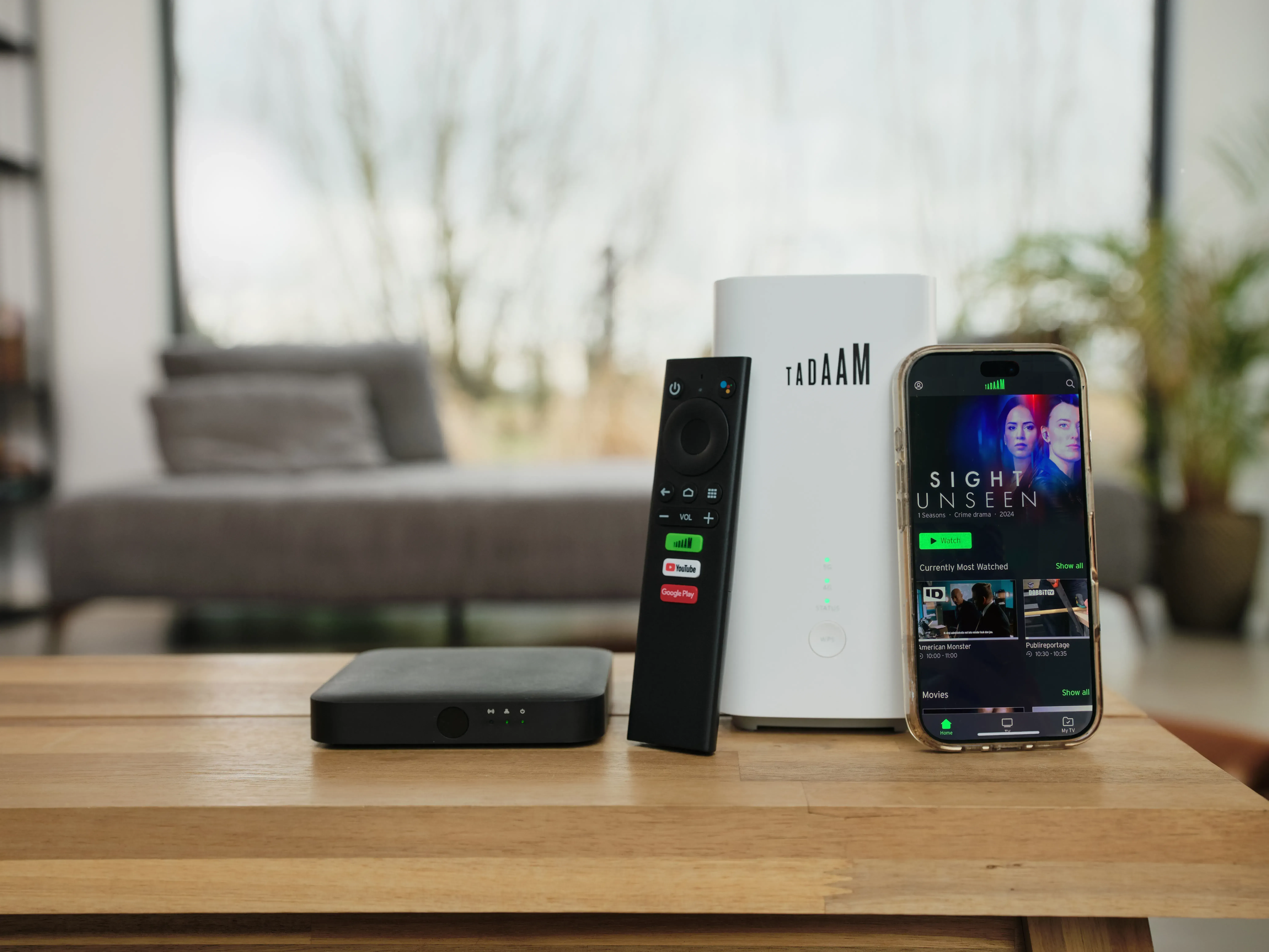 Modem TADAAM, TV box et télécommande posés sur une table à côté d'un smartphone affichant l'application TADAAM TV.